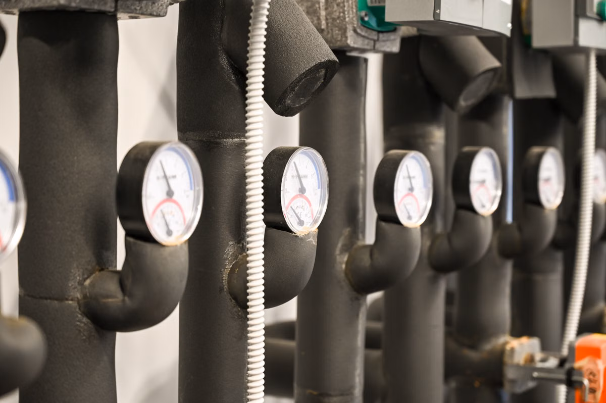 A row of insulated heating pipes fitted with temperature gauges in a plant room.